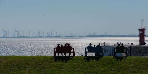 Rear view of silhouette people sitting on bench by sea against clear sky