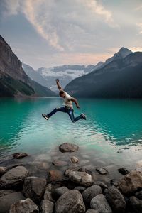 Full length of man jumping on rocks by lake against mountains