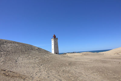 Lighthouse by building against clear blue sky