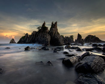 Rocks on beach against sky during sunset