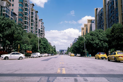 Cars on city street by buildings against sky