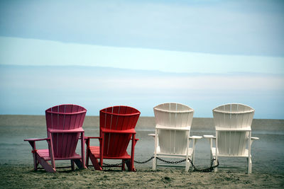 Empty chairs on beach against sky