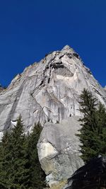 Low angle view of rocky mountain against clear blue sky