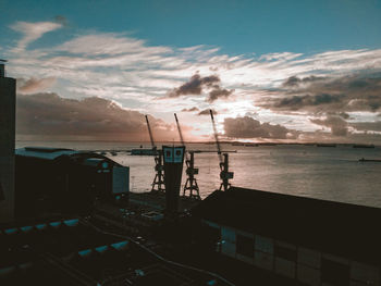 Sailboats in sea by buildings against sky during sunset