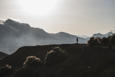 Silhouette man walking on ridge against sky