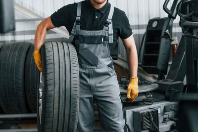 Walking and holding tyre. man in uniform is working in the auto service.