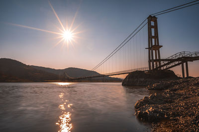 Suspension bridge over bay against sky during sunset