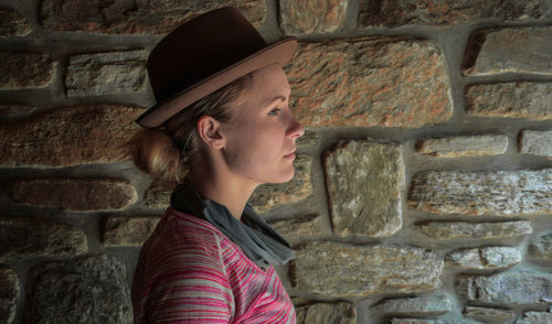 Profile view of young woman standing against brick wall