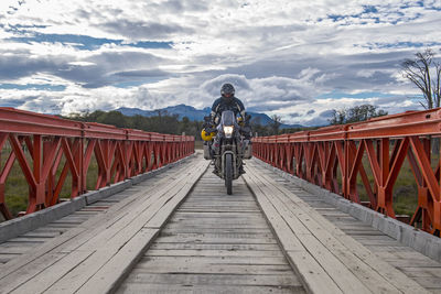 Man on off road touring motorbike crossing wooden bridge