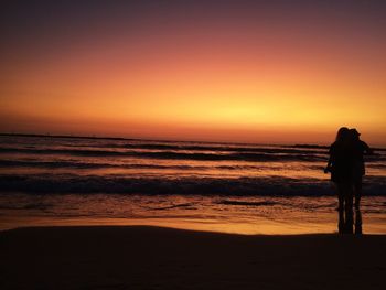 Silhouette woman standing on beach against sky during sunset