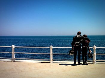 Couple enjoying view of sea while standing on promenade against clear sky