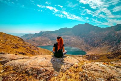 Woman sitting on rock against sky