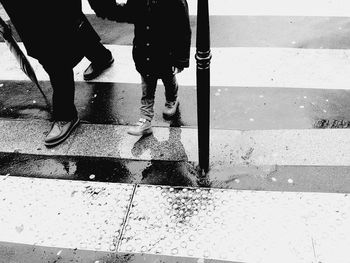 Low section of father and son walking on zebra crossing during rainy season