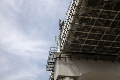 Low angle view of crane by building against sky