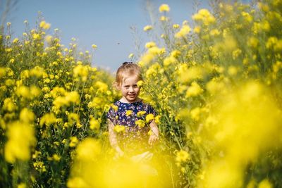 Portrait of girl amidst yellow flowers at oilseed rape field