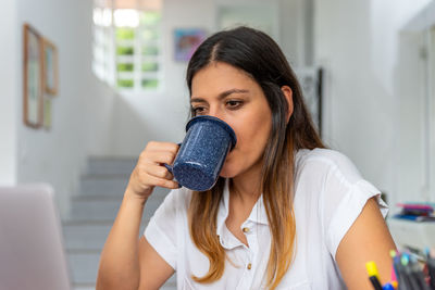 Portrait of young woman holding camera at home