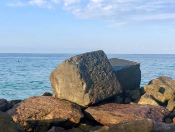 Rocks on shore by sea against sky