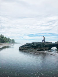 Side view of man standing on rock against sky