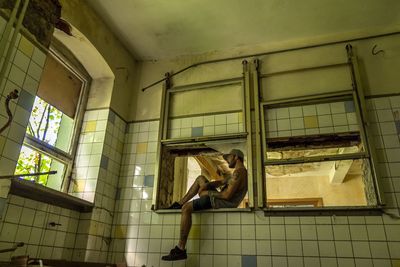 Full length of hipster sitting on window frame in abandoned building