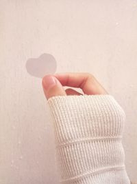 Cropped hand of woman holding heart shape against wall