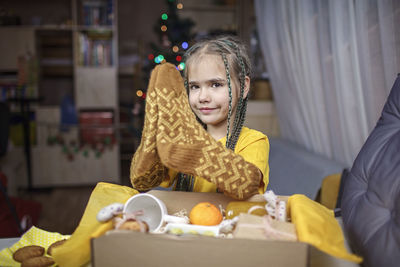 Girl packing care box with tea, honey, cookies and knitted wool socks for grandmother on christmas