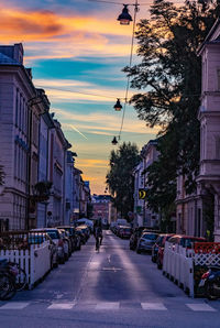 City street by buildings against sky during sunset