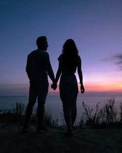 Silhouette couple holding hands while standing against sky during sunset