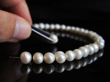 Cropped hand making pearl necklace over table