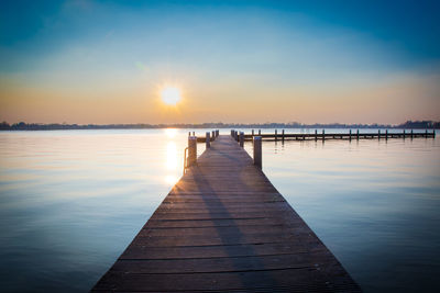 Pier on lake against sky during sunset