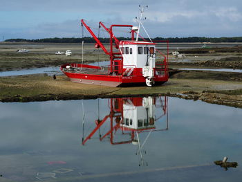 Red fishing boat moored at beach against sky