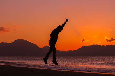 Silhouette man on beach against orange sky