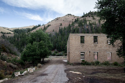 Empty dirt road by abandoned building against mountain