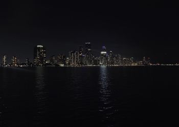 Illuminated buildings by sea against sky at night