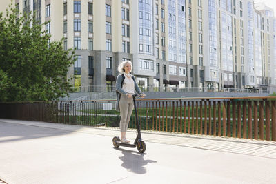 Woman riding electric push scooter at street on sunny day