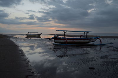 Boat moored on beach against sky during sunset