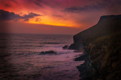 Scenic view of sea and cliffs against sky during sunset