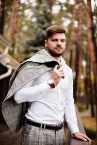 Young man looking away while standing by railing against trees in forest