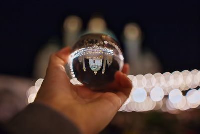 Close-up of cropped hand holding crystal ball with reflection at night