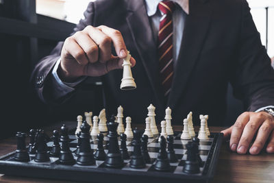 Midsection of businessman playing chess at table