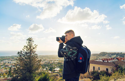 Man photographing with camera standing against sky