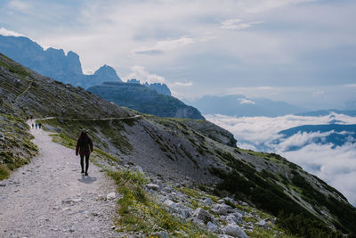 Rear view of man walking on mountain against sky