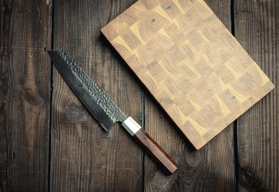 Metal kitchen knife and wooden cutting board on a table made of brown wooden boards, top view