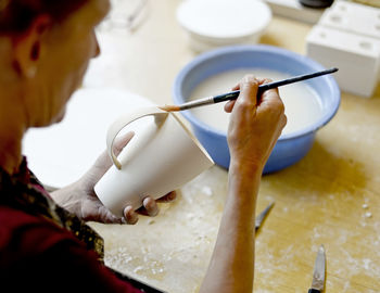 Woman using brush on mug in porcelain workshop