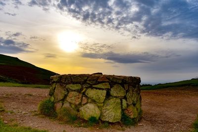 Stone wall on field against cloudy sky