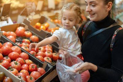 Woman with girl buying tomatoes at supermarket