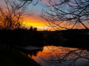 Silhouette trees by lake against romantic sky at sunset