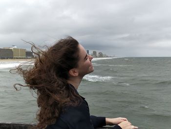 Young woman standing at beach against sky