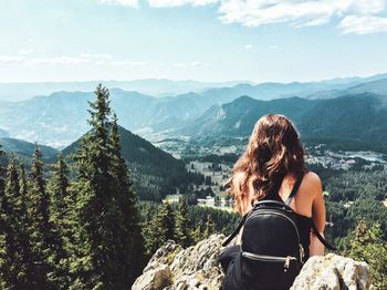 Rear view of woman sitting on cliff against mountains