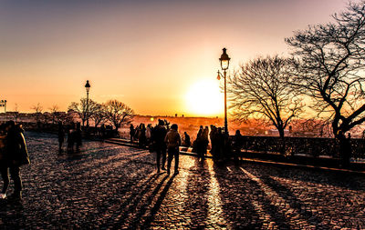 Silhouette people walking on street against sky during sunset