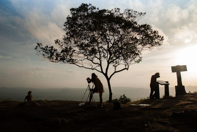 Silhouette man photographing by tree against sky during sunset